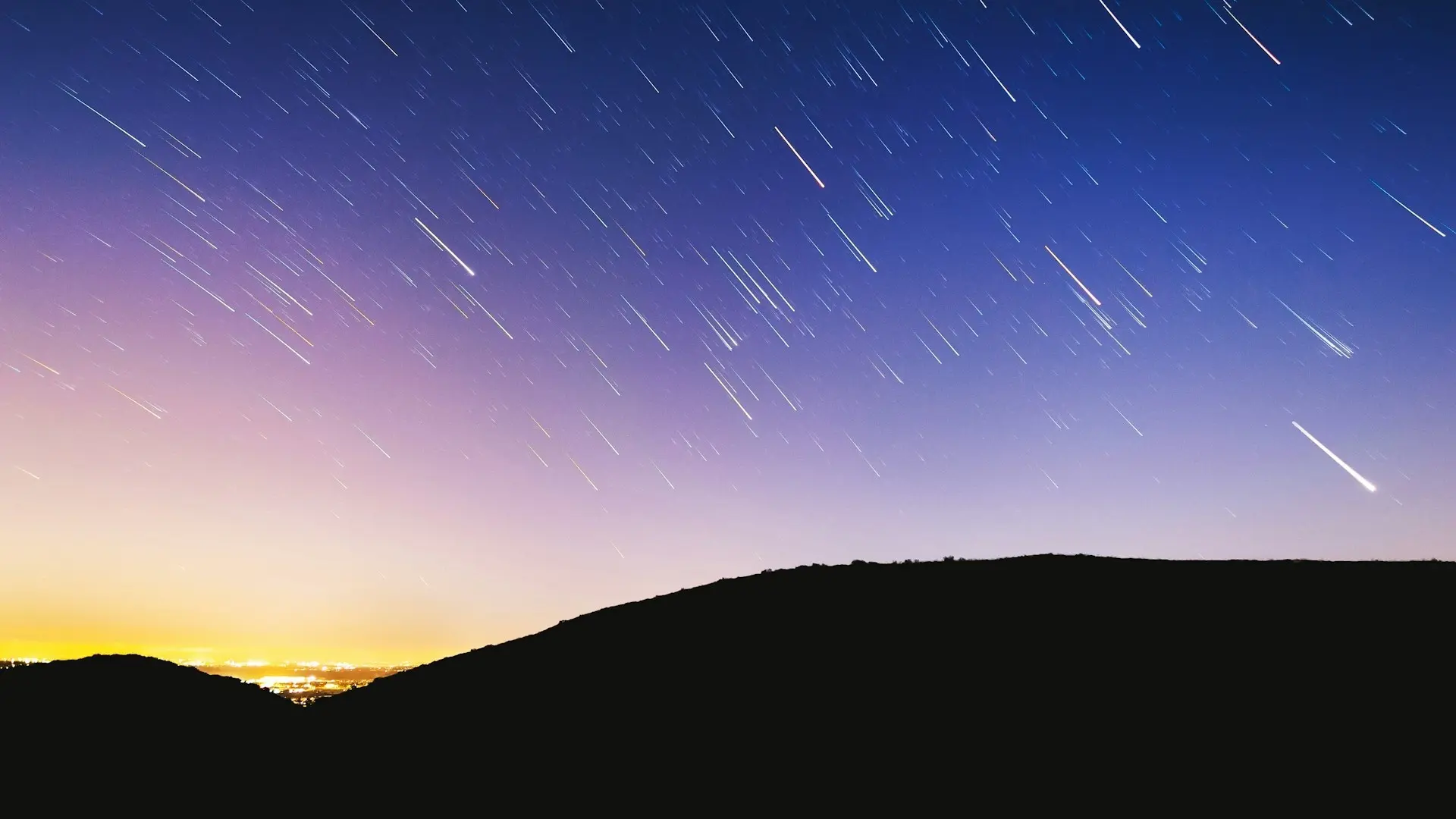 Una persona observando la lluvia de estrellas Perseidas en un campo oscuro, lejos de la ciudad.