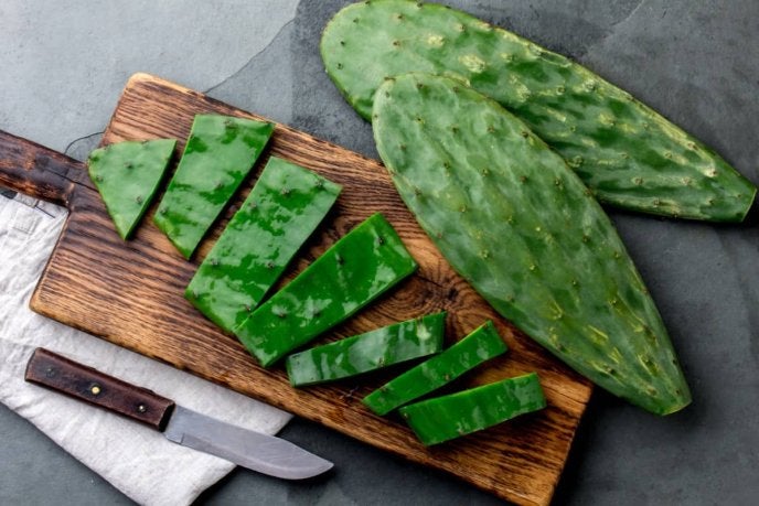 Una persona cortando nopales frescos en una tabla, preparándose para aplicar un truco sobre cómo quitar la baba a los nopales.
