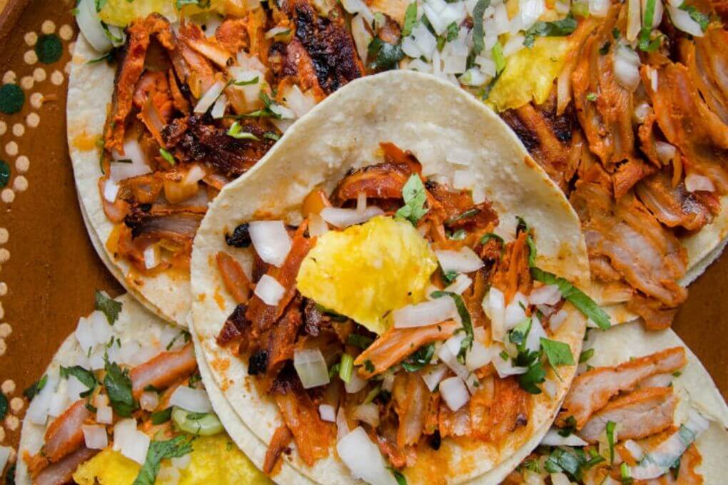 Plato de tacos al pastor con piña, cilantro y cebolla, representando uno de los tacos más populares en México.