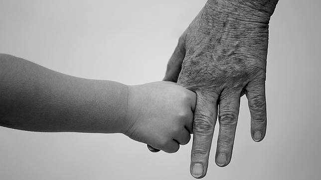 Manos de abuelos y su nieto entrelazadas, representando el vínculo eterno incluso con los abuelos fallecidos.