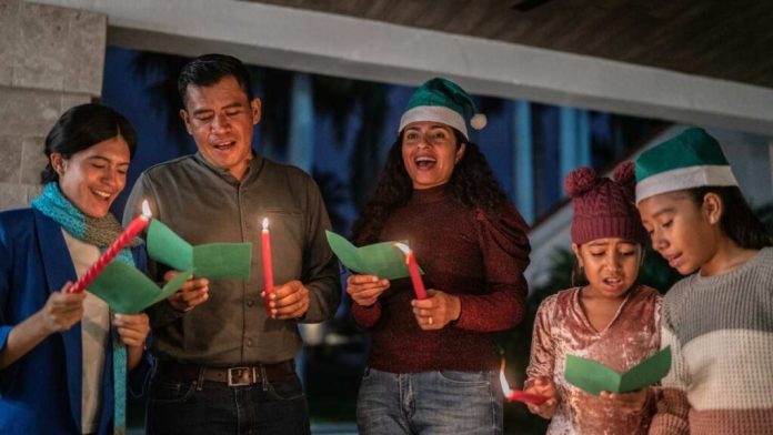 Personas en una procesión de posada, llevando un nacimiento y velas, cantando la letanía para pedir posada.