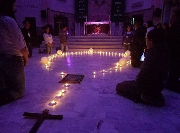Personas rezando un rosario durante un novenario, con velas y una imagen religiosa.