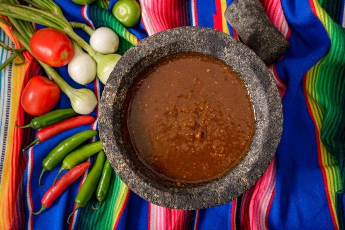 La receta de salsa para barbacoa servida en un molcajete junto a tacos de barbacoa.