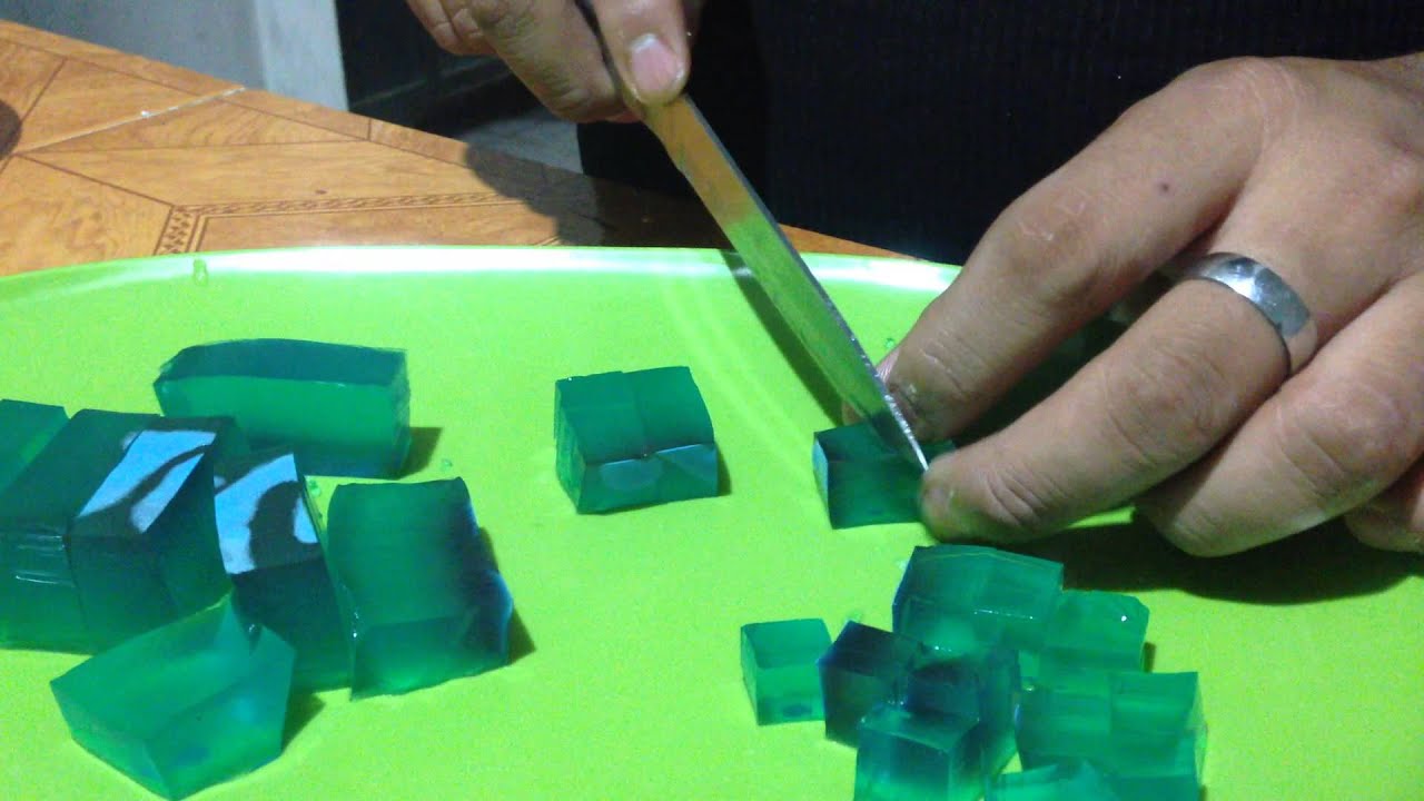 Manos cortando cubos de gelatina de colores en un recipiente, parte de la preparación.