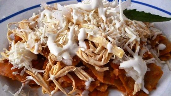 Plato de chilaquiles rojos con pollo, queso, crema y cebolla, listo para degustar.