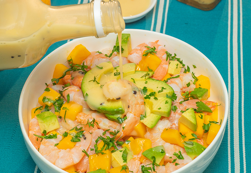 Un tazón de vidrio con la receta de ceviche de mango terminada, decorado con aguacate y cilantro.