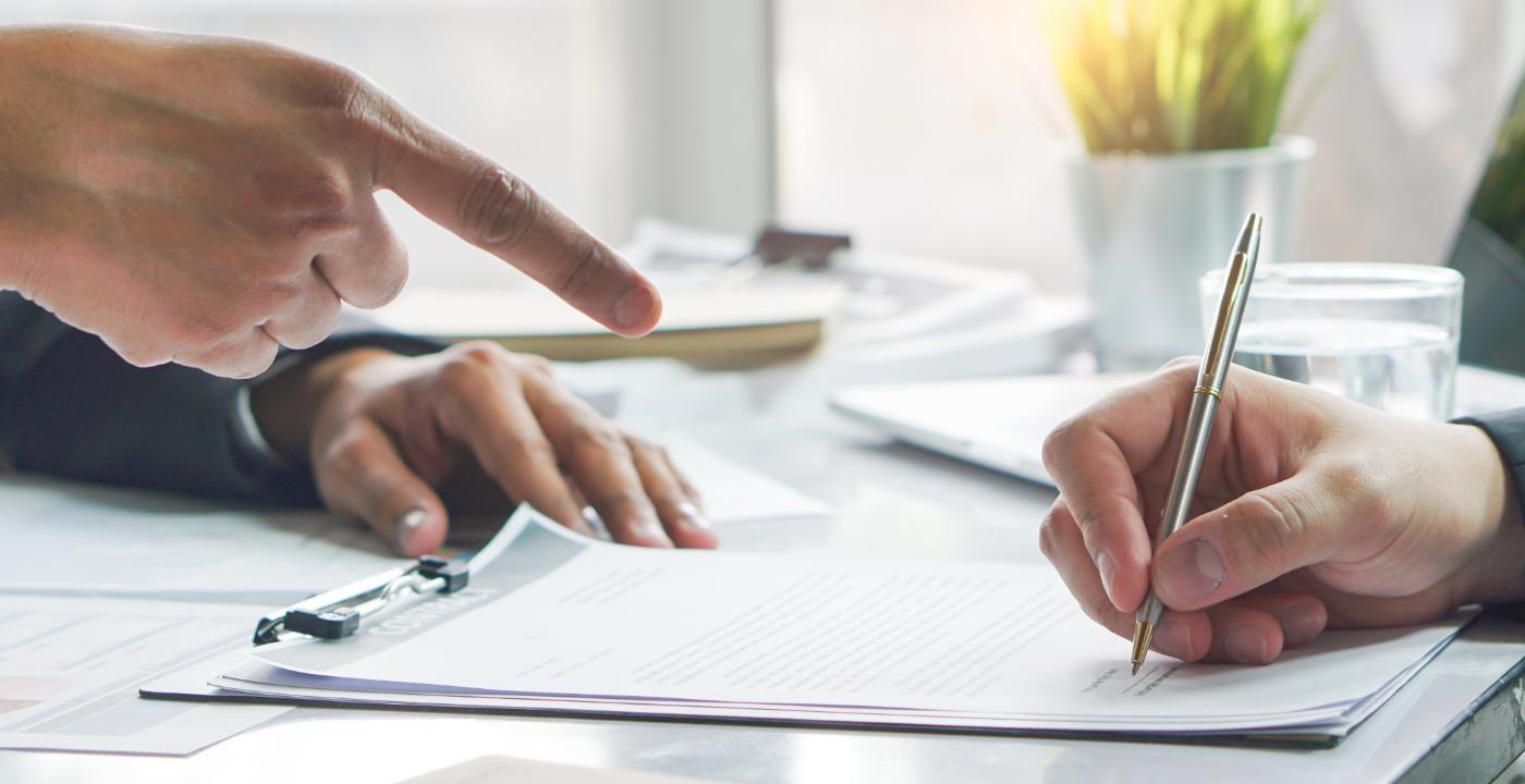 Una mano leyendo un contrato con un lápiz rojo, simbolizando la precaución al firmar documentos durante Mercurio Retrógrado.