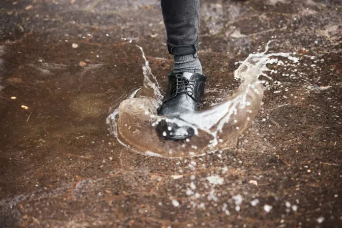 Pies con zapatos sucios caminando por un charco de lodo negro.