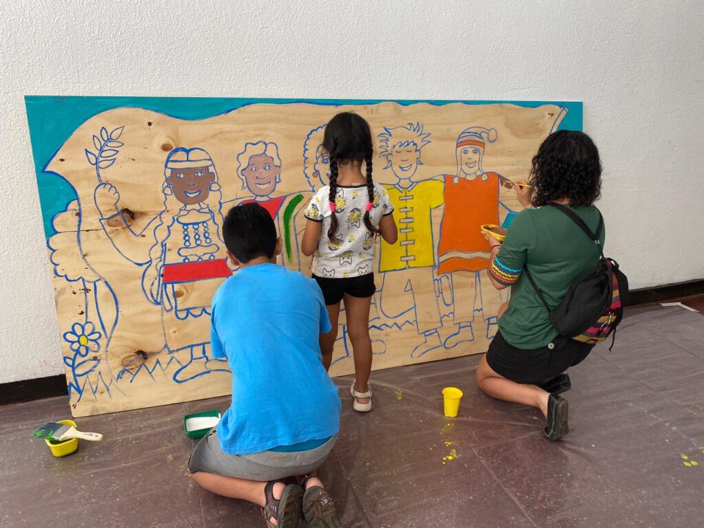 Niños pintando mural colectivo en papel kraft con pinturas de colores en calle cerrada de la colonia Roma CDMX durante Día del Niño